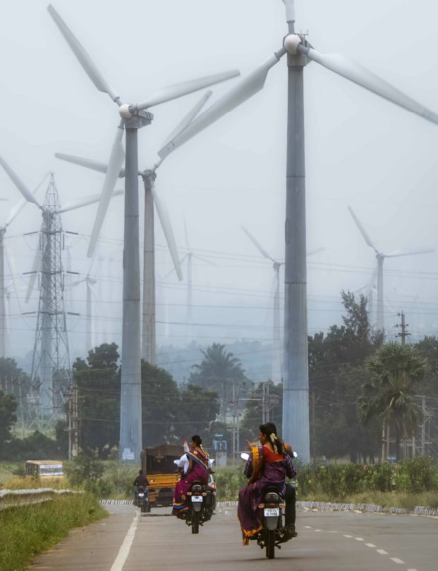 Bikes in India ride past a field of modern windmills 